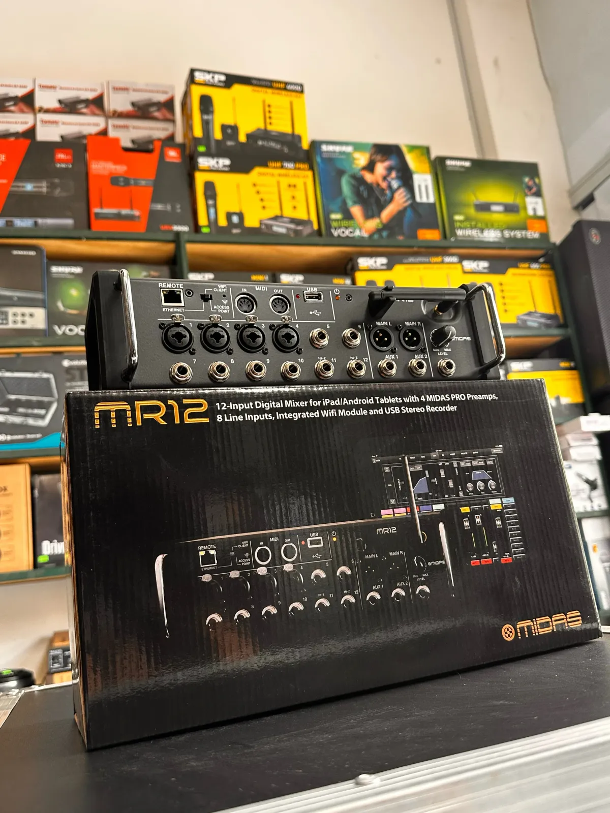 La Midas MR12 es una mezcladora digital de 12 canales diseñada para estudios y aplicaciones en vivo, controlada a distancia a través de una aplicación para tabletas (iPad o Android), PC y Mac. Su diseño portátil tipo "caja de escenario" integra un enrutador Wi-Fi para un control inalámbrico sin necesidad de equipos externos. 